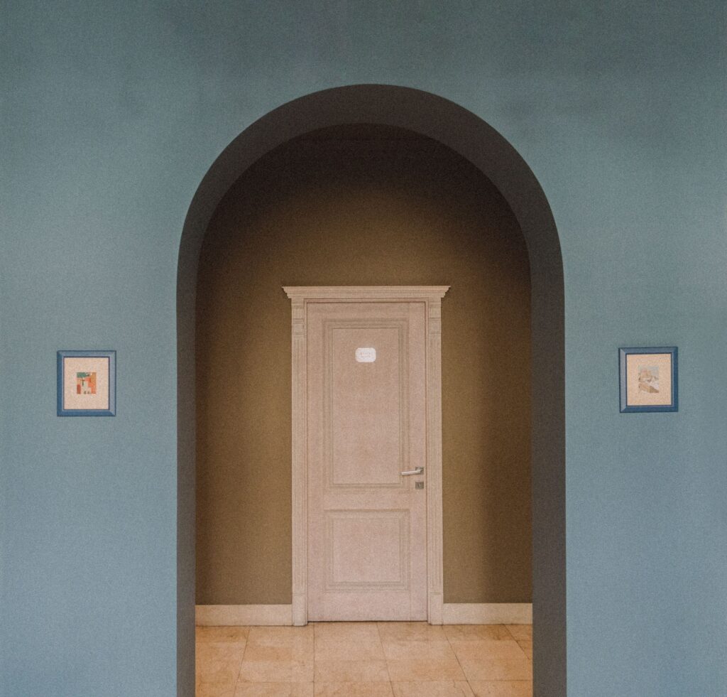 Interior focus on an archway leading to a classic door, flanked by framed artwork.