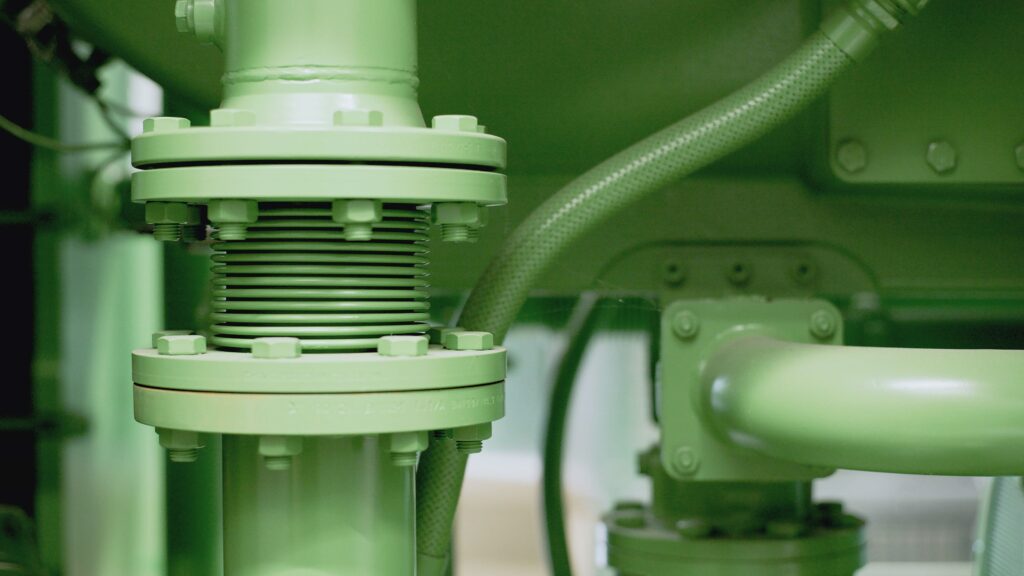 Detailed view of a green industrial pipe and valve system in a mechanical setting.